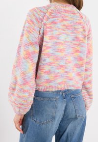 Pull en tricot à coupe décontractée, arborant des teintes pastel de rose, bleu et jaune. Tissu texturé et détails de ourlet côtelé. À associer avec un jean bleu.