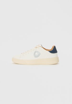 White sneaker with a smooth leather upper, cream rubber sole, tan leather accents, and a circular logo on the side. Navy heel detail.