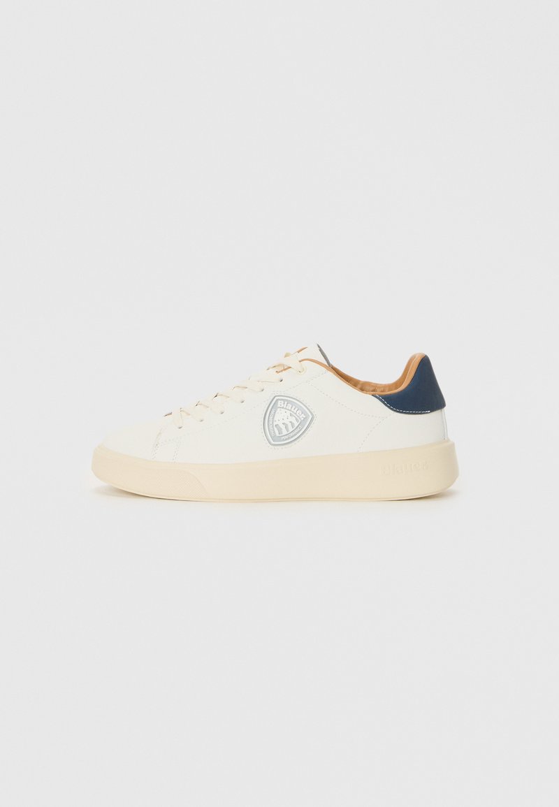Sneaker alb cu un superior din piele netedă, talpă din cauciuc crem, accente din piele maro și un logo circular pe lateral. Detaliu pe călcâi de culoare bleumarin.