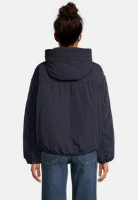 Doudoune marine à capuche, avec un ourlet froncé et des poignets élastiques. Texture lisse avec un léger éclat, conçue pour la chaleur et le confort.