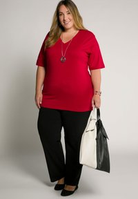 Maglietta rossa a V con maniche corte, abbinata a pantaloni neri e ballerine nere. Porta una borsa a due tonalità, in pelle bianca e nera. Presente una collana d'argento.