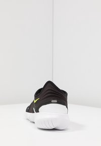 Czarne buty sportowe z teksturowanym wierzchem, białą wkładką i zielonym akcentem. Posiadają design zapewniający stabilne dopasowanie, okrągły czubek oraz elastyczną podeszwę.