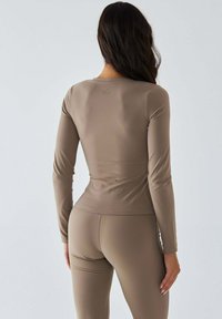 Langärmliges braunes Sportoberteil aus glattem, dehnbarem Stoff; figurbetontes Design mit rundem Ausschnitt und dezentem Logodetail auf der Rückseite.