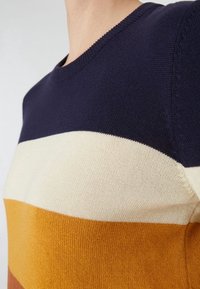 Stickad tröja med horisontella ränder i marinblått, krämfärgat och senapsgult. Rundad halsringning och medelgrovt stickat mönster med en figursydd design.