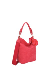 Sac à épaule en suede rouge avec une bandoulière réglable et une étiquette ronde attachée, présenté sur un fond blanc.