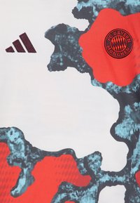 Camisa de Adidas con una base blanca, patrones abstractos en azul y rojo, acentos texturizados y el logo del FC Bayern München en el centro.