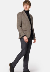 Brązowa marynarka w kratę z wyłogami, na dwa guziki i kieszeniami bocznymi, w połączeniu z dopasowanymi ciemnoszarymi spodniami w kratę oraz czarnymi botkami za kostkę.