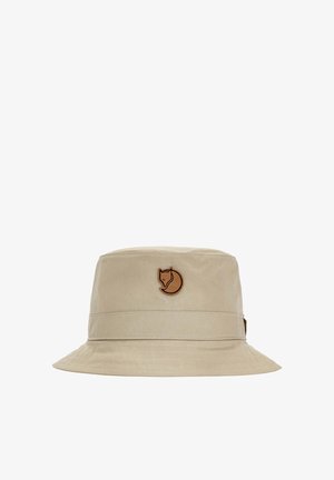 Beige bucket hat met brede rand en een bruin vos-logo patch in het midden aan de voorkant.