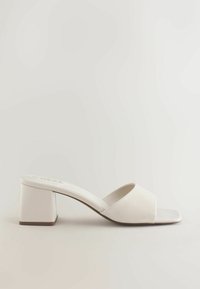Sandale mule à petit talon bloc en cuir lisse ivoire, avec un bout ouvert et une large bride au-dessus du pied.