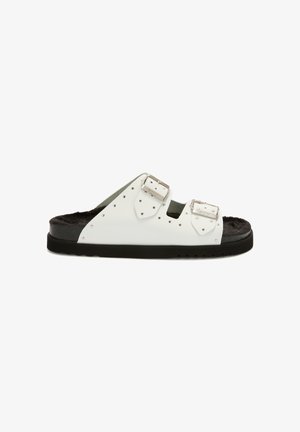 Sandale blanche à glissière avec deux boucles en argent, semelle intérieure en fourrure noire rembourrée et semelle en caoutchouc noir striée, vue de profil.