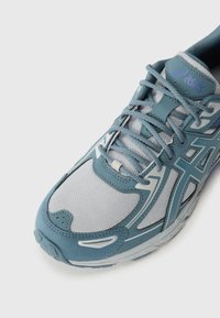 Light blue athletic shoe with a mesh upper and synthetic overlays. Features a padded tongue, laces, and a textured sole for grip.
