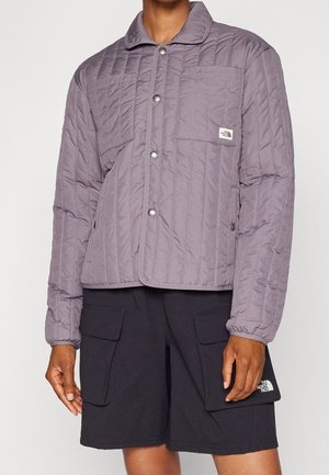 Persona que lleva una chaqueta acolchada color malva con botones y pantalones cortos cargo negros con bolsillos con solapa, ambos de la marca The North Face.