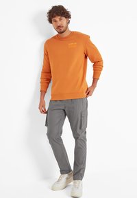 Orange crewneck sweatshirt with embroidered text paired with gray cargo pants featuring side pockets and beige sneakers.