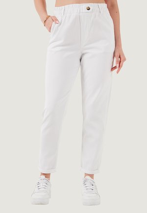 White, elastic-waist pants with a button detail, side pockets, tapered legs, and rolled cuffs, worn with white sneakers on a light background.