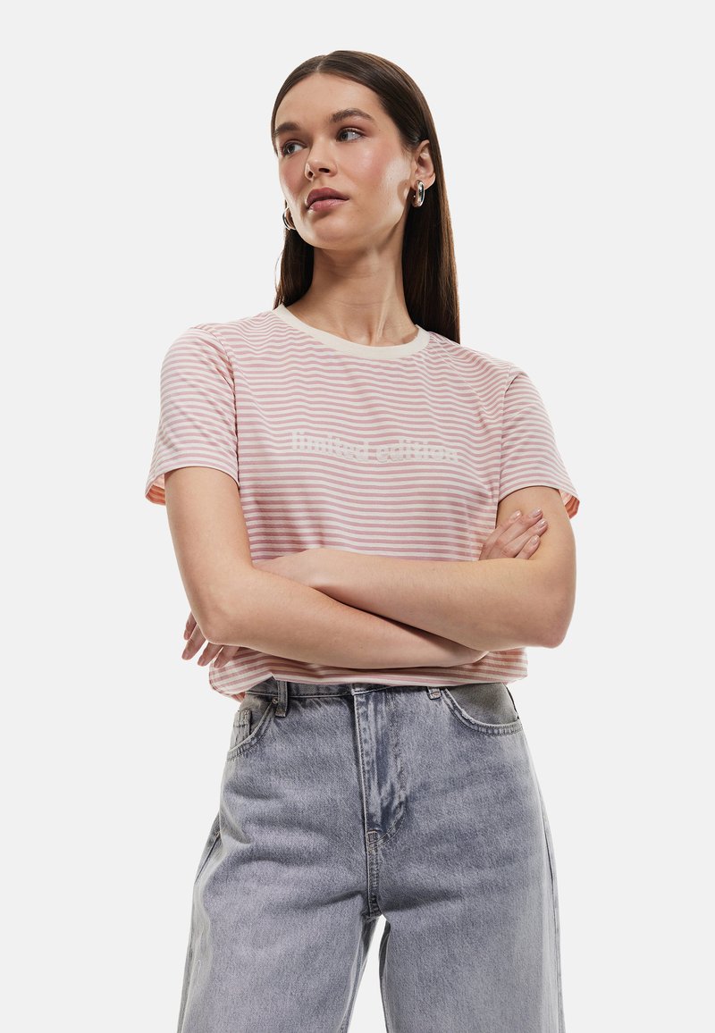 Lyserødstribet kortærmet T-shirt med rund hals og hvid skrift, parret med højtaljede lyse denim jeans. Glat stoftekstur.
