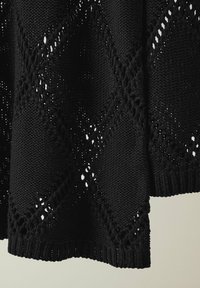 Schwarzer Strickpullover mit einem strukturierten Muster und ausgeschnittenen Rautenformen, gerippten Bündchen und lockerer Passform.