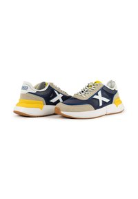 Navy and beige sneakers with a yellow accent, featuring mesh and suede materials, white logo, and textured rubber sole. Laced design.