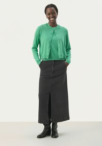 Grön stickad cardigan med knappar fram, kombinerad med en svart denim maxikjol med mittslits. Svarta ankelboots fulländar outfiten.