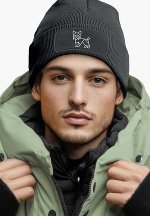 Black ribbed knit beanie with a textured finish, featuring a white embroidered dog design on a rectangular patch, worn with a green puffer jacket.