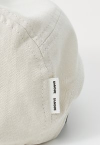 Beige cotton cap with a textured finish. Features stitched seams and a visible white label reading "SAMSØE" on the side.