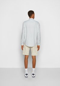 Camicia a maniche lunghe a righe blu chiaro e bianche, abbinata a pantaloni cargo beige. Indossata con calzini bianchi e scarpe da ginnastica con dettagli navy.