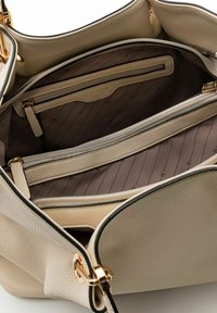 Borsa a tracolla in pelle beige con texture, aperta per mostrare diversi scomparti con zip e un rivestimento in tessuto marrone chiaro con un motivo sottile.