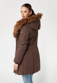 Rudas paminkštintas paltas su dirbtiniu kailiniu apykakle, kapišonu ir šoninėmis užtrauktuko kišenėmis. Ant peties yra logotipo morceau, o rankogaliai yra banguoti.