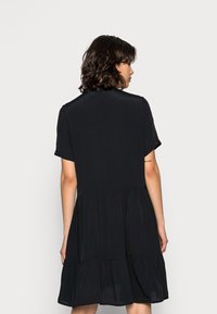 Vestido preto de manga curta com um design em camadas, apresentando um corte solto e um tecido suave. A vista traseira revela um decote simples e arredondado.