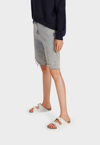 Infradito bianchi con due cinturini regolabili a fibbia, una soletta testurizzata e una suola leggera, abbinati a pantaloni shorts in denim scoloriti.