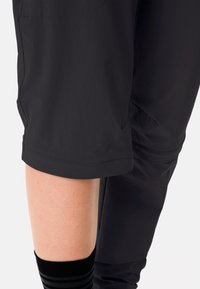 Pantaloni sportivi neri realizzati in tessuto liscio, con orli cuciti e una tasca laterale, abbinati a un calzino nero con strisce grigie.