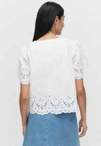 Vit bomullsblus med puffärmar, spetsdetaljer längs fållen och scalloped kant. Bärs med en blå denimkjol.