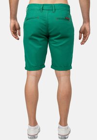 Pantaloni corti in cotone verde con una vestibilità slim, orli risvolti e due tasche posteriori. Presentano cuciture a contrasto e un'etichetta sulla vita.