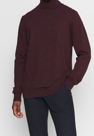 Burgunderfarbener Rollkragenpullover, Strickstoff, lockere Passform, gerippte Bündchen und Saum, kombiniert mit dunkel gemusterten Stoffhosen.