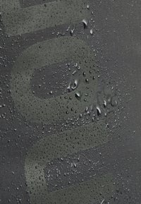 Grijs stof met grote reliëfletters, voorzien van waterdruppels, die de waterbestendige textuur en capaciteit benadrukken.