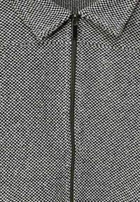 Teksturowana czarno-biała kurtka zapinana na zamek, z kołnierzem i centralnym zamkiem błyskawicznym. Materiał ma pleciony wzór z kontrastującymi kolorami.