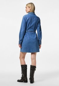 Rochie din denim albastră cu guler, talie cu curea și mâneci lungi. O pereche de cizme negre până la genunchi cu catarame și toc gros.