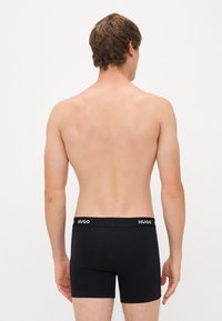 Boxeri negri dintr-un material elastic, cu un tiv logoat și o finisare netedă. Designul este ajustat, oferind o siluetă simplă.