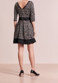 Robe noire à fleurs avec un dos en V, des manches trois quarts, une taille cintrée, une jupe évasée et un ourlet noir. Associée à des talons noirs avec des accents argentés.