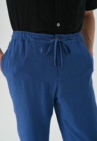 Blauwe katoenen broek met een elastische tailleband en trekkoord. Voorzien van zijzakken en een gladde textuur met subtiele kreukels.