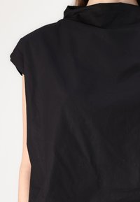 Top senza maniche nero con colletto alto, realizzato in un tessuto leggero e testurizzato. Finitura liscia con dettagli di cucitura visibili.