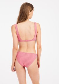 Roze prugasti bikini set izrađen od teksturiranog materijala. Ima široke naramenice i nisku leđa. Donji dio ima srednji kroj i usklađen dizajn.