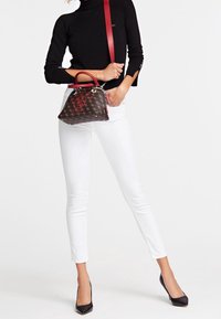 Brązowa torebka w wzory z czerwonymi akcentami, srebrnym okuciem i górnym uchwytem. Połączona z białymi ciasnymi spodniami i czarnymi szpilkami z ostrym noskiem.