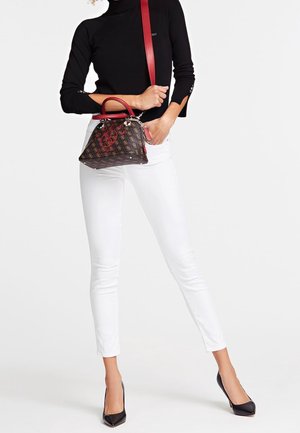 Bruine handtas met een patroon en rode accenten, zilveren hardware en een bovenhandvat. Gecombineerd met witte skinny jeans en zwarte pumps met een spitse neus.