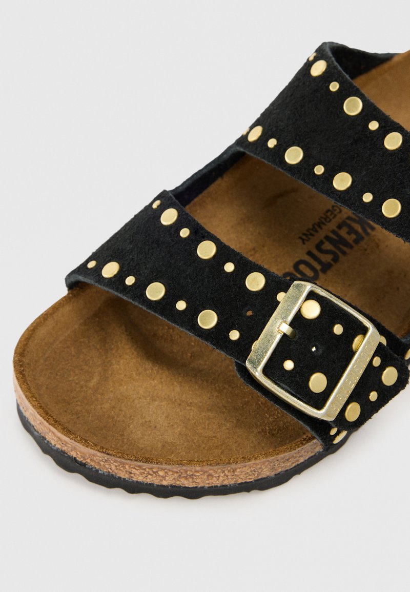 Zwarte suède sandaal met gouden studs, twee brede banden en een metalen gesp. Kurken zool met een gestructureerde voetbed.