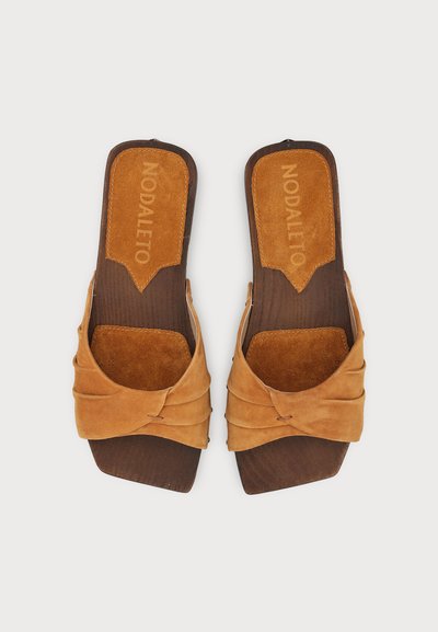Paire de sandales en daim marron à enfiler avec des brides torsadées et des semelles carrées en bois, marquées ""Nodaleto"" sur la semelle intérieure.