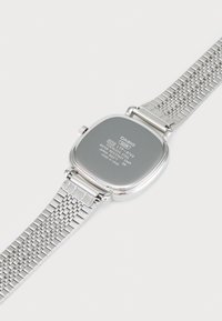 Montre Casio en acier inoxydable avec un boîtier carré, un bracelet en maille et le dos gravé affichant les spécifications. Couleur argentée avec une texture lisse.