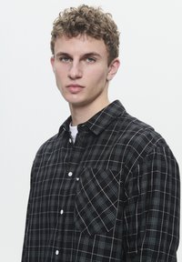 Black and white checkered shirt with a button-up design, featuring a pocket on the left chest and a soft fabric texture.
