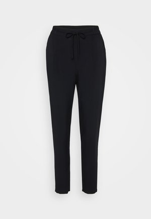 Mustad mustad püksid elastse vöökohtaga, tõmblukuga ja kitsenevate jalgadega. Valmistatud pehmest kangast, millel on sile tekstuur.