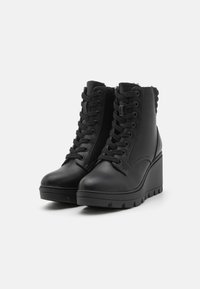 Bottines en cuir noir avec un talon compensé, présentant un laçage à l'avant, des détails texturés sur les côtés et une semelle en caoutchouc épaisse.