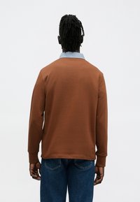 Bruine trui met een blauwe denim kraag, lange mouwen en een gladde textuur, gecombineerd met blauwe denim jeans. Achteraanzicht weergegeven.